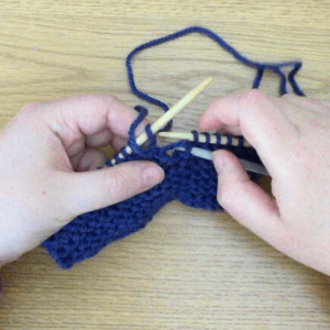 hands holding knitting using a third needle to catch a dropped stitch