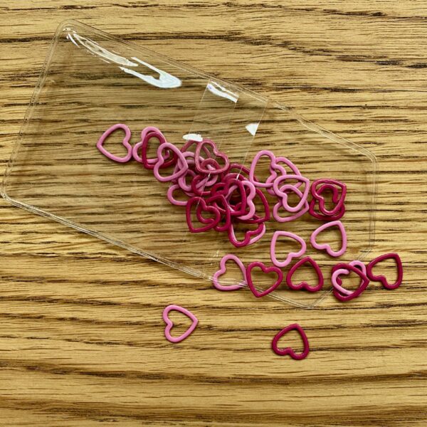 Pink heart shaped stitch markers falling out of plastic packaging on table