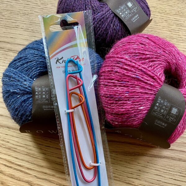 Pack of 3 knitters stitch holders on table with three balls of yarn, link blue and purple