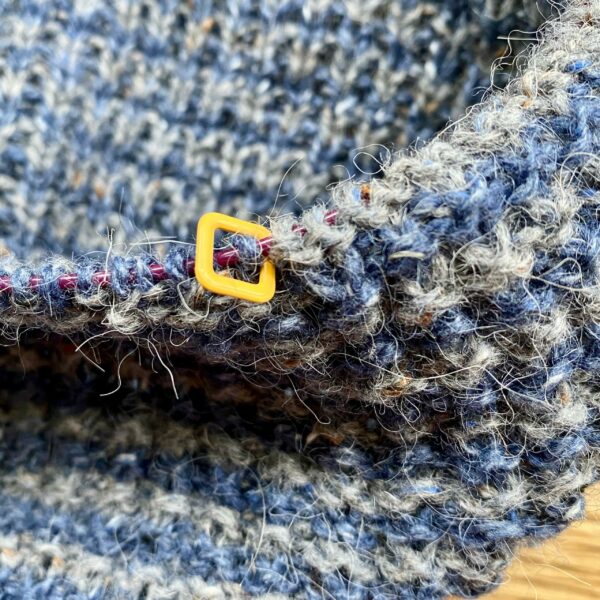 yellow square stitch marker on knitting needle with blue and grey knitting